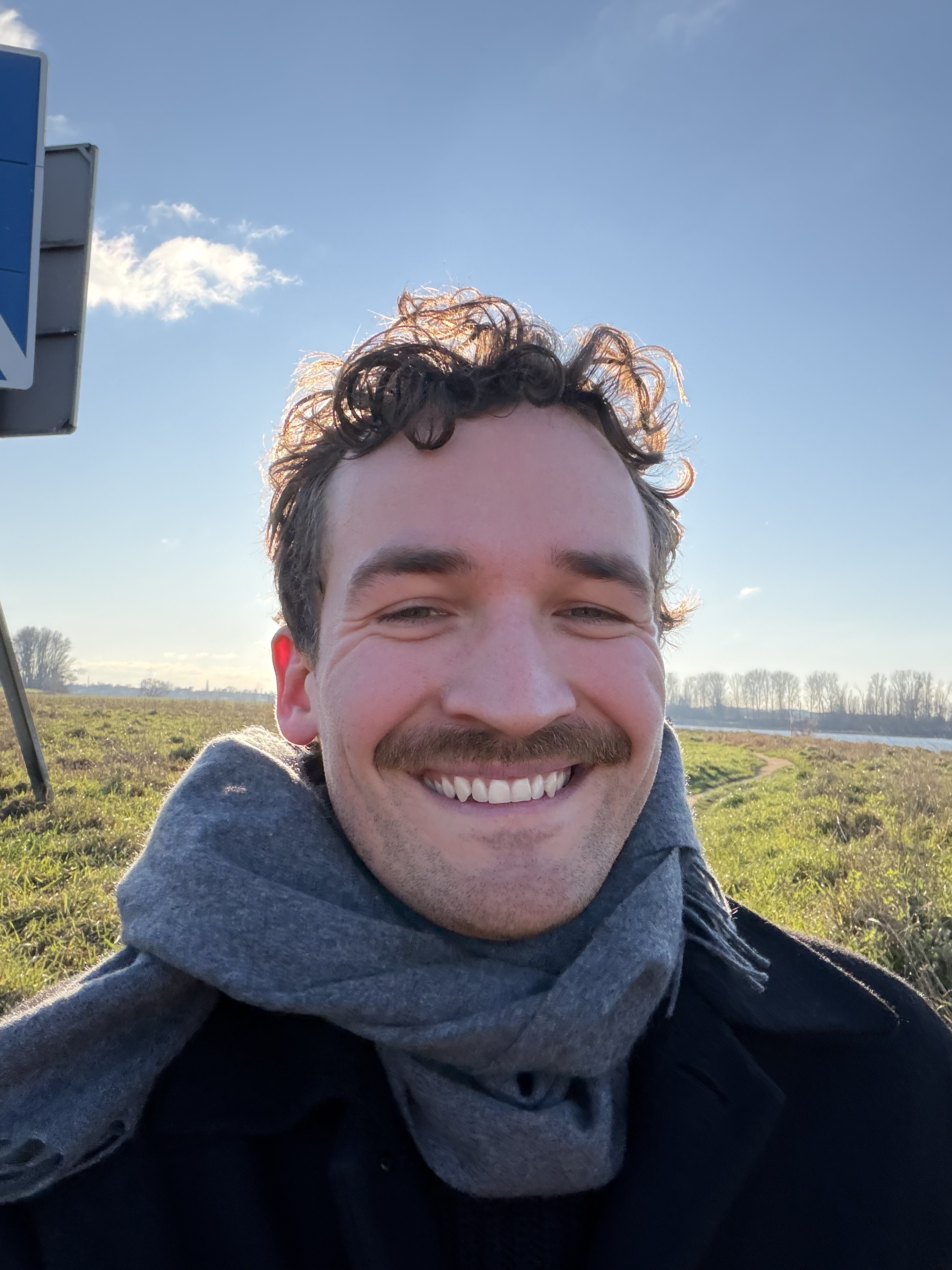 Julian Simon smiling outdoors along the Rhine near Cologne